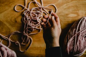 A detailed view of a pink yarn ball held by a hand on a warm wooden surface.